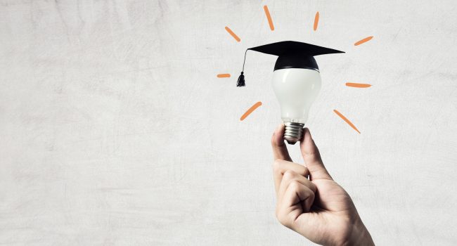 Hand of businessman holding glowing light bulb with graduation hat on it